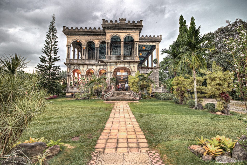 The Ruins in Talisay, Negros Occidental, a roofless mansion of pale columns and arches at the end of a brick path with palms on both sides.