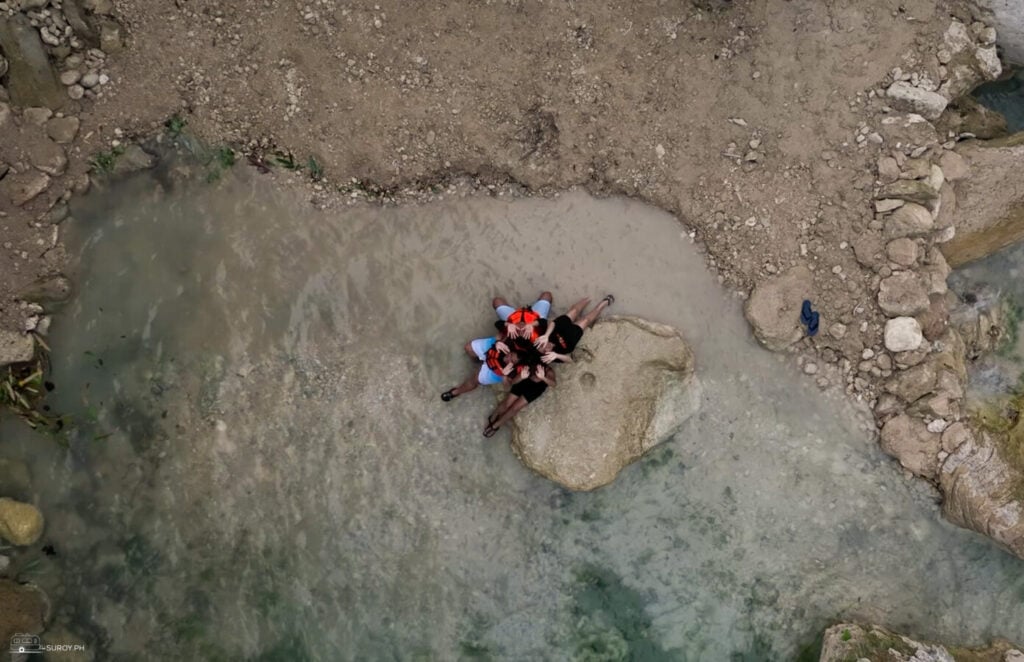 A wide shallow section of the Inambakan river running gray and silty over a rock shelf after rain