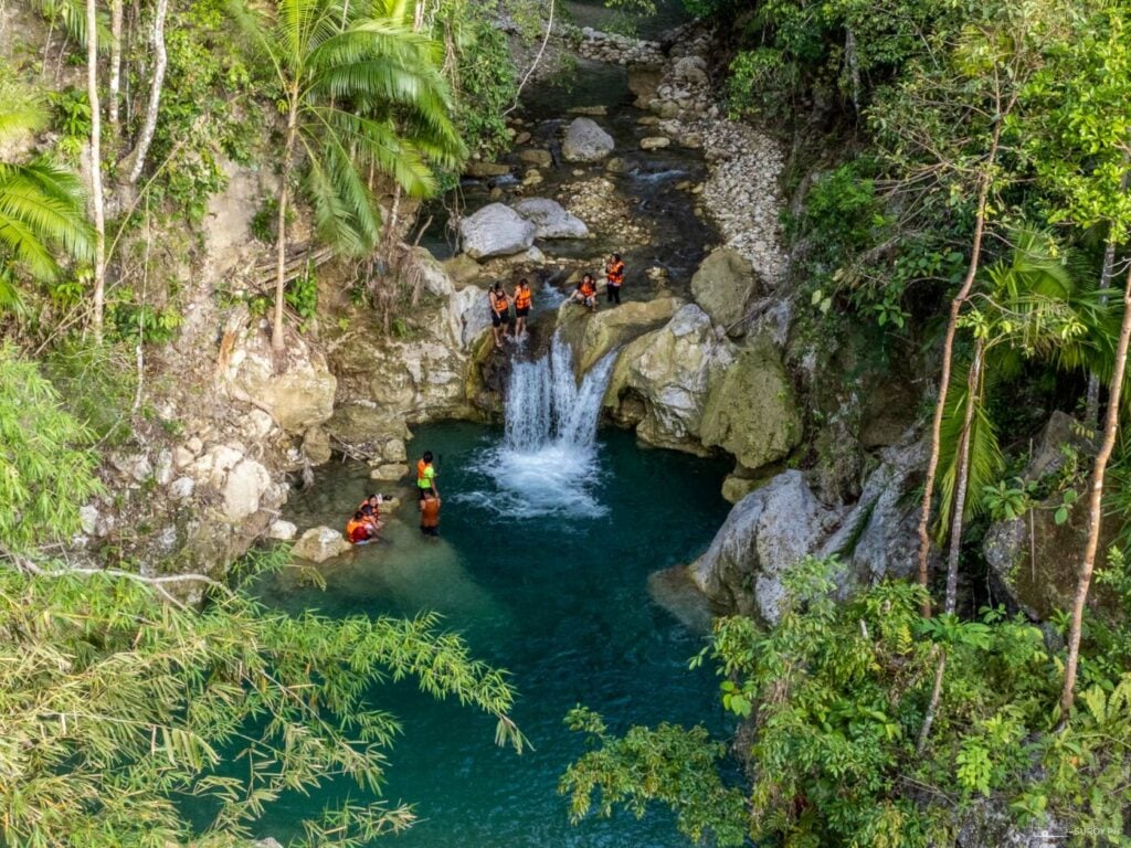 Swimmers in orange life vests in the turquoise pools of the upper tiers at Inambakan Falls