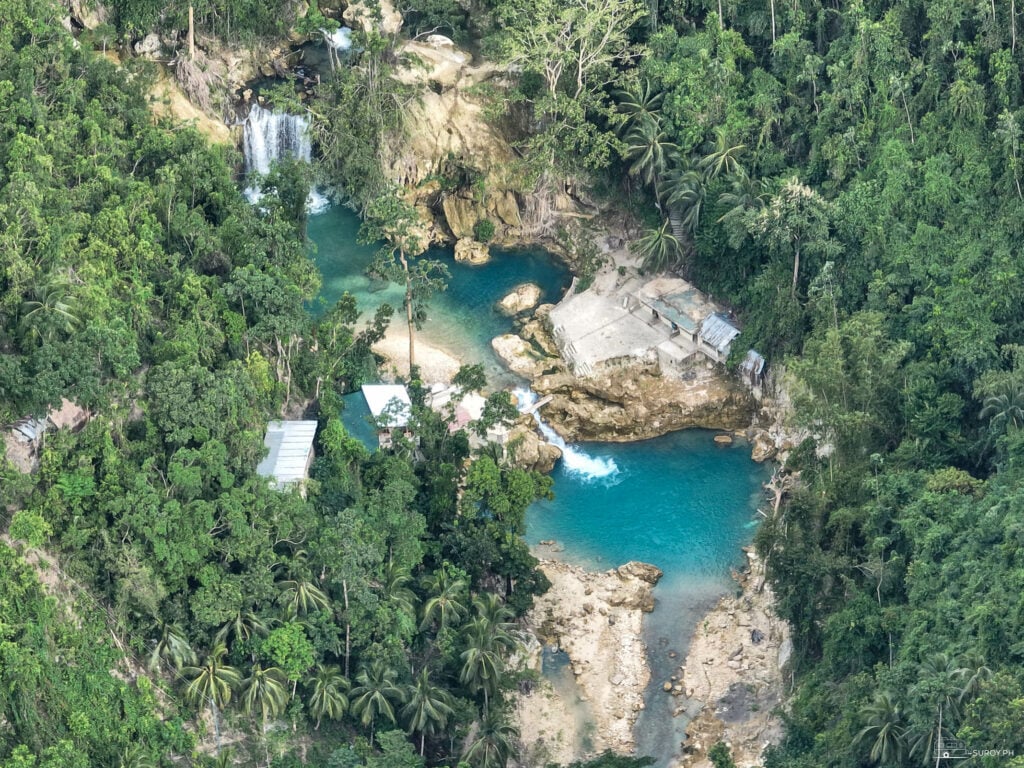 An aerial shot of the highest of the three waterfalls that make up Kawasan Falls, along with its turquoise blue water. 