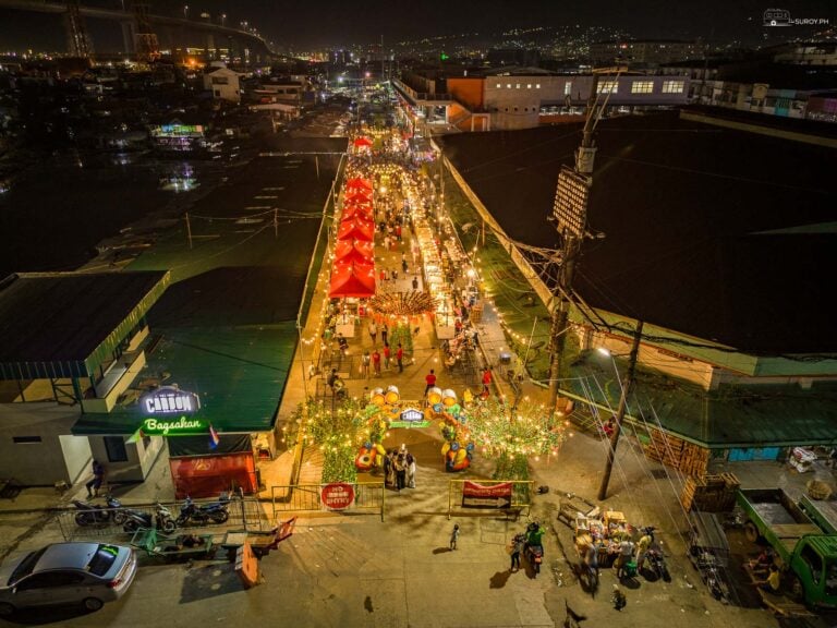 Carbon market in Cebu City at night seen from above, a long avenue of lit stalls with vehicles and traders along both sides.