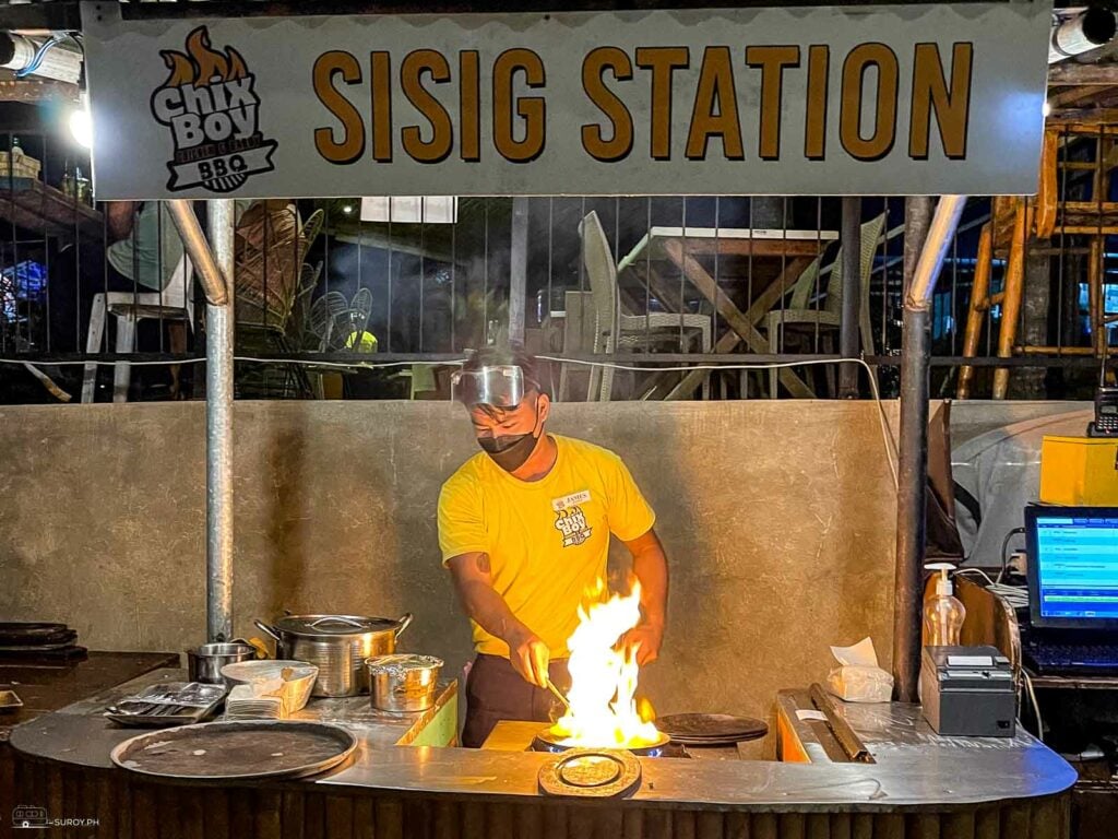 A chef prepares the food at the sisig station. 