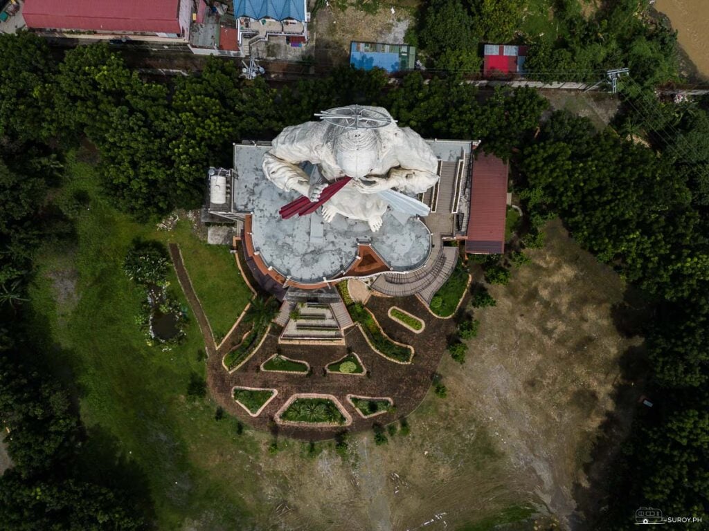 A top-down aerial shot of the Divine Mercy Statue in Bulacan and the Rosary Hill Grotto of Our Lady of Lourdes, where people pray for healing.