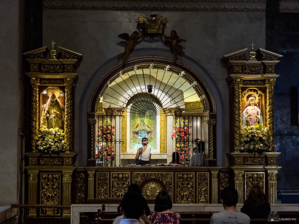 Devotees gather in prayer before the ornate altar adorned with images of saints and intricate gold details.