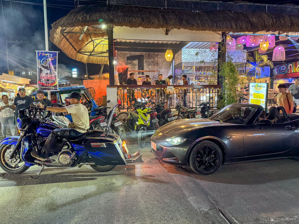 Nightlife along a busy street in Basdiot, Moalboal, with people and motorcycles outside bars and restaurants.