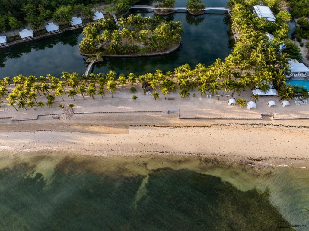 An aerial view of the resort’s pristine beach, crystal-clear waters, and lush palm trees, inviting you to unwind and relax.