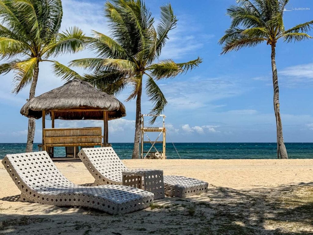 Relax on the beach with comfortable lounge chairs and a thatched hut.