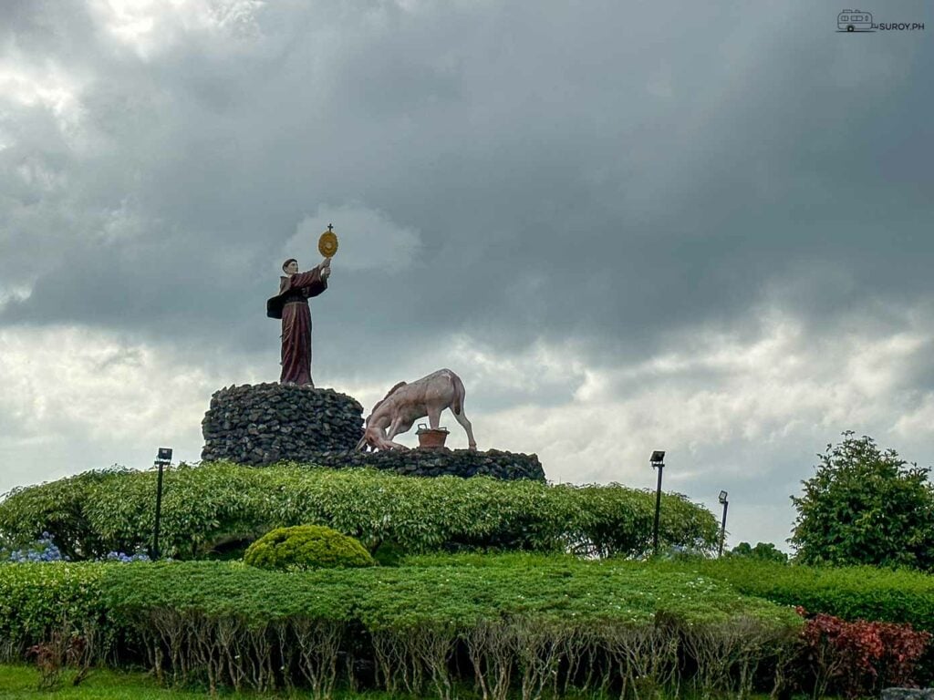 A Statue of Devotion: A priest stands tall amidst the lush greenery and under dramatic skies, offering a powerful symbol of faith and reverence in Roxas City