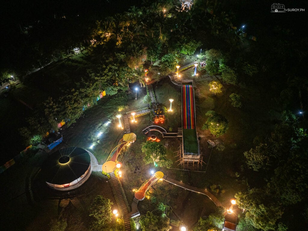 A nighttime view of Aya’s Hill amusement park showcases its attractions and pathways illuminated by a kaleidoscope of colors.