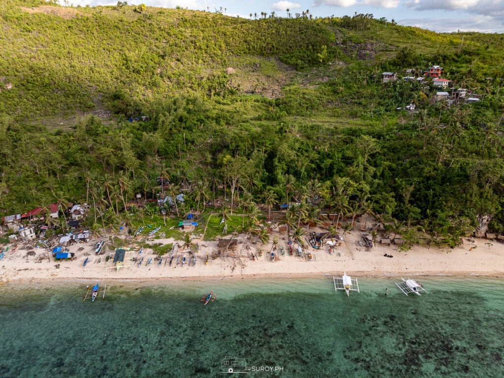 A serene aerial view of Hermit’s Cove, a hidden gem in Cebu, nestled between lush green hills and crystal-clear waters. Perfect for those seeking tranquility and a natural escape.