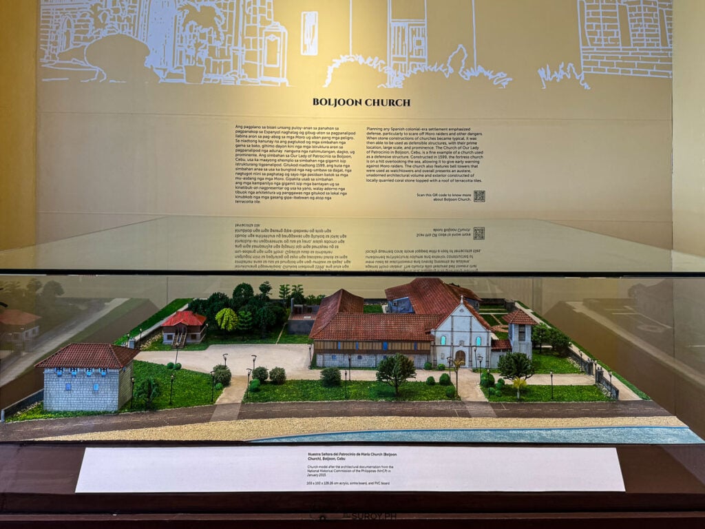 A scale model of Boljoon Church in a glass case under a wall of text