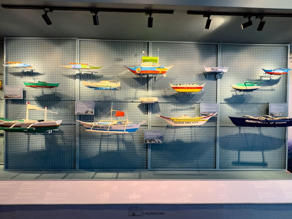 Model boats from different Cebu towns lined up on shelves against a gray wall