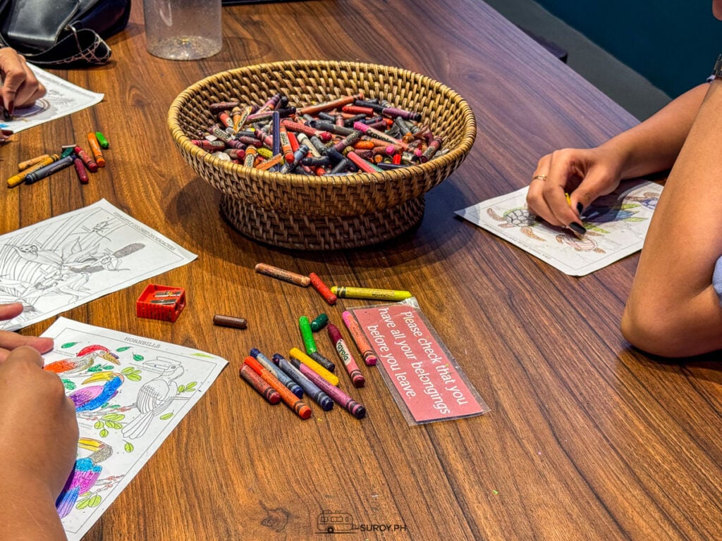 Children coloring at a wooden table with a basket of crayons