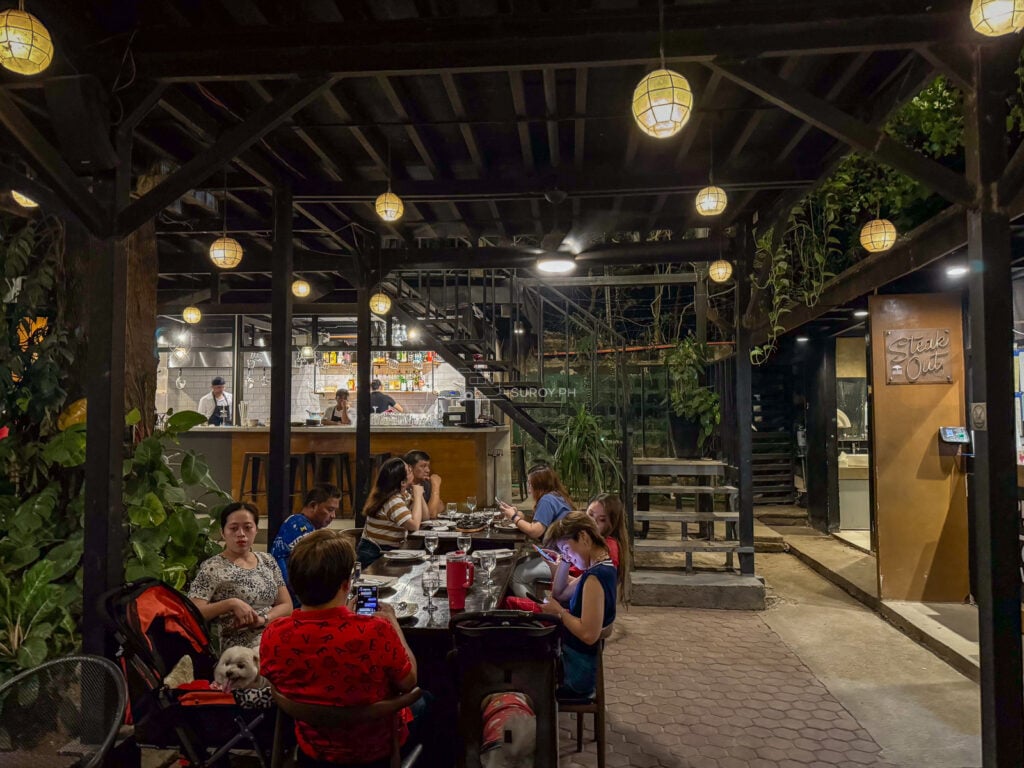 The open sided timber pavilion at Acacia Steakhouse Cebu with hanging globe lights and diners at long tables