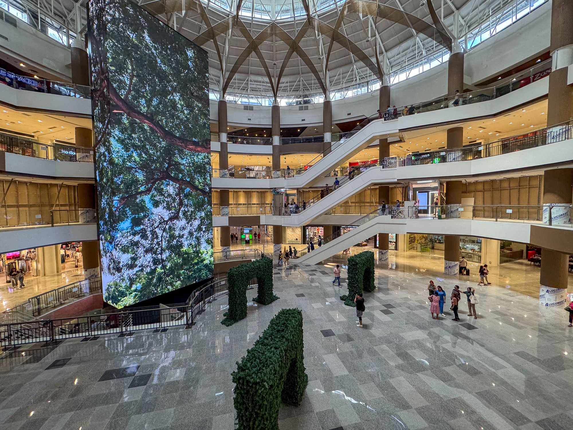 The renovated activity center of Ayala Center Cebu: granite floor, greenery arches, and the four-storey LED column under the dome.