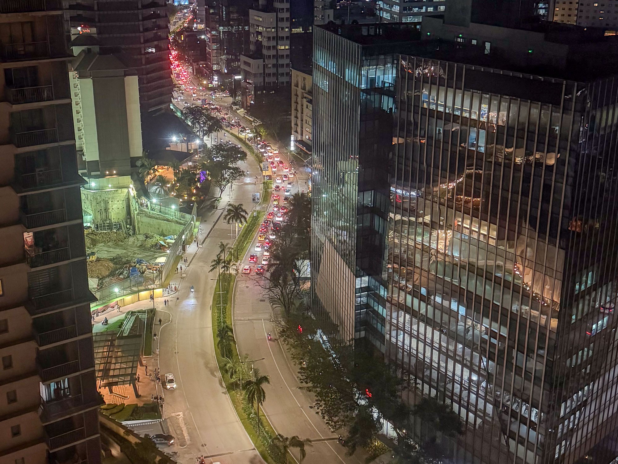 Night view over Cebu Business Park with the Ayala Center Cebu expansion site behind hoarding in the lower left and traffic queued along the avenue.