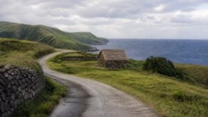 Curving road, stone house, green hills, and sea in a Batanes-inspired landscape