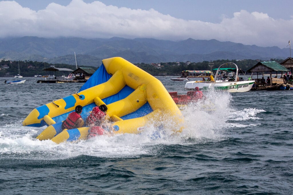 A yellow and blue flying fish inflatable lifting off the water at speed with riders holding on, off Boracay