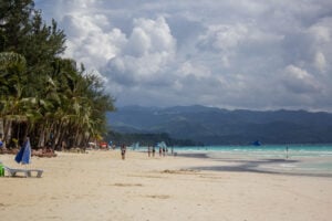 Wide palm-lined section of Boracay White Beach beneath large clouds
