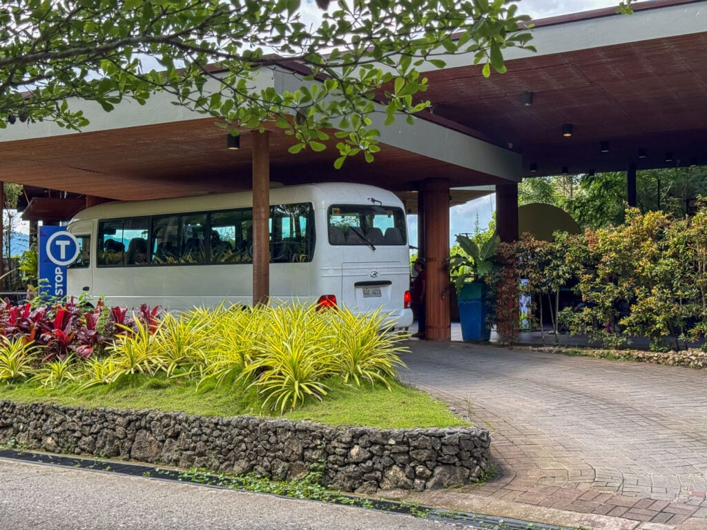A white shuttle bus parked under a covered drop-off with landscaped planting at Cebu Safari and Adventure Park