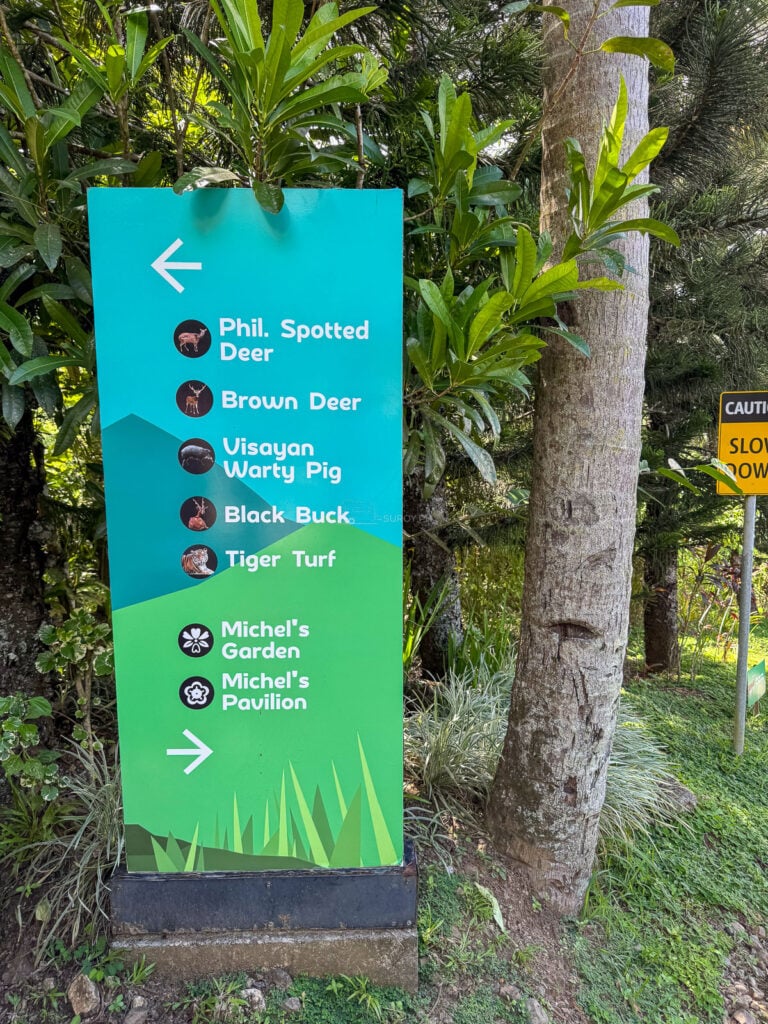 A green wayfinding signpost listing Philippine spotted deer, brown deer, Visayan warty pig, black buck, Tiger Turf, Michel’s Garden and Michel’s Pavilion