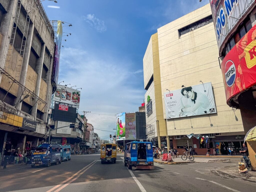 Metro department store on Colon Street viewed past an older multi-storey building with jeepneys and cars in traffic between