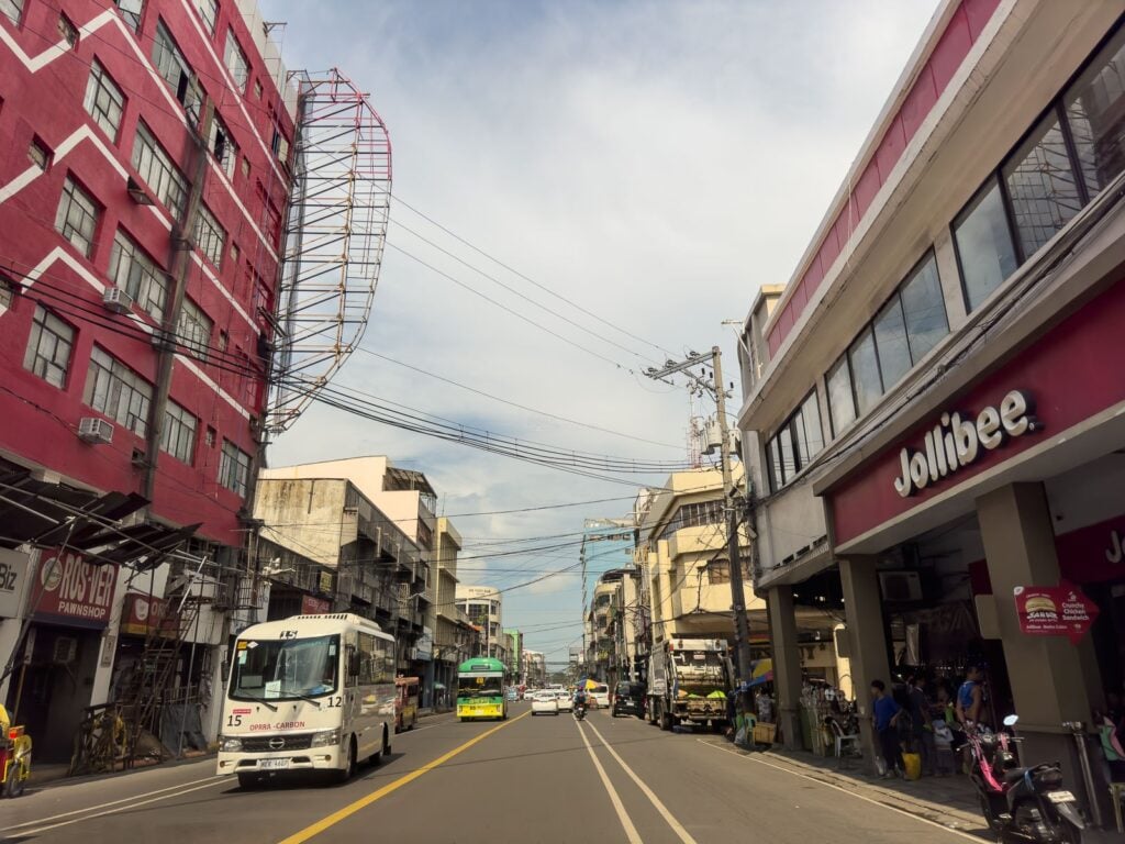 Street-level view of Colon Street with a red apartment building on the left, a Jollibee branch on the right and a bus in the middle lane