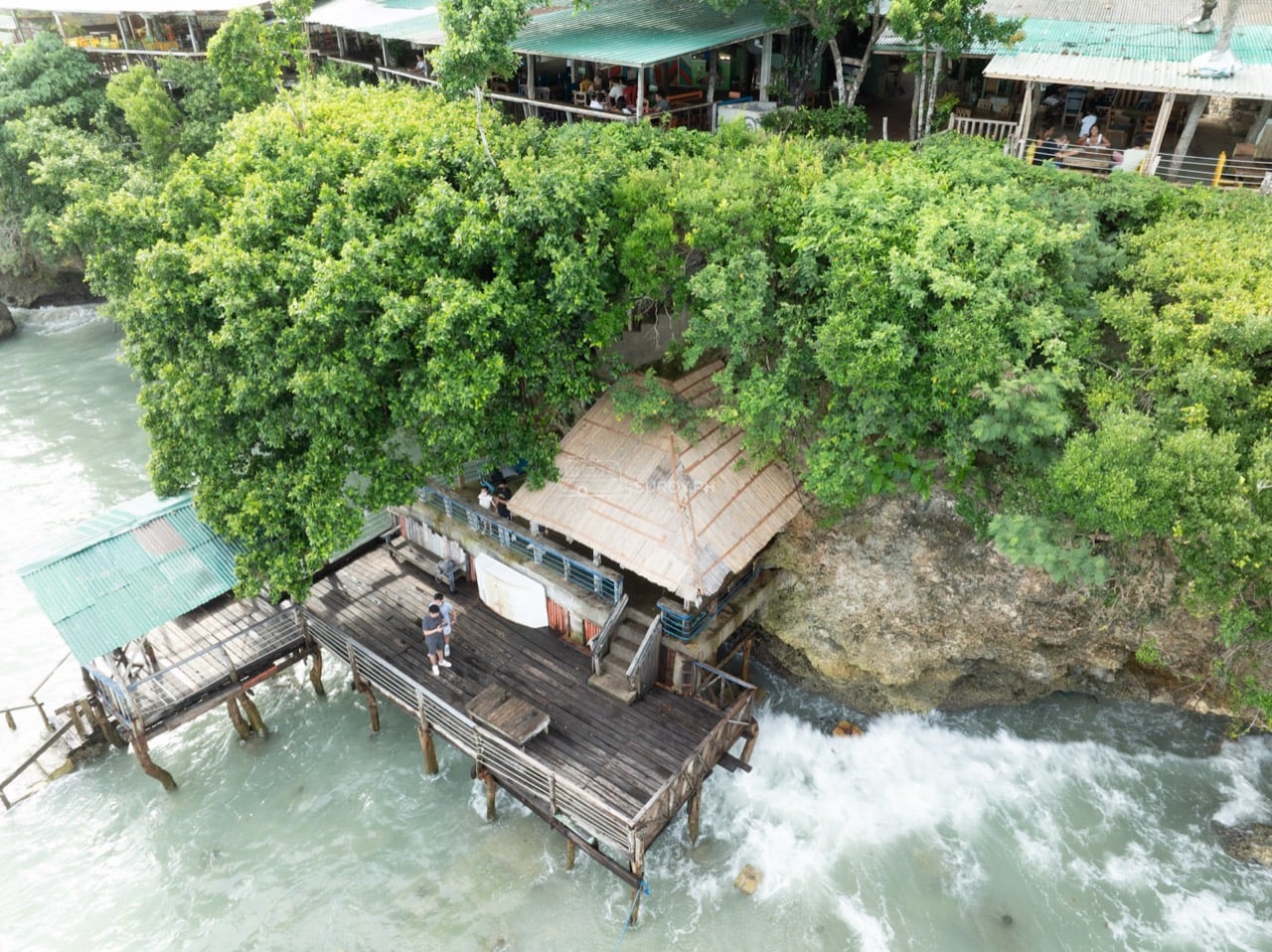 Aerial view of a wooden waterfront deck below trees and restaurants on Panglao Island