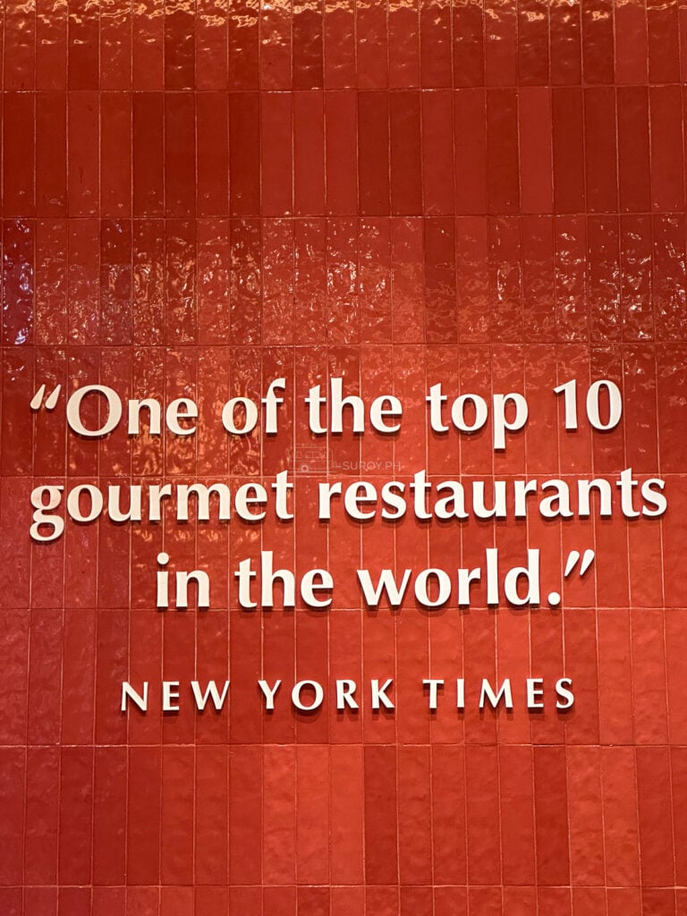 A framed New York Times line on the red wall at Din Tai Fung calling it one of the top ten gourmet restaurants in the world