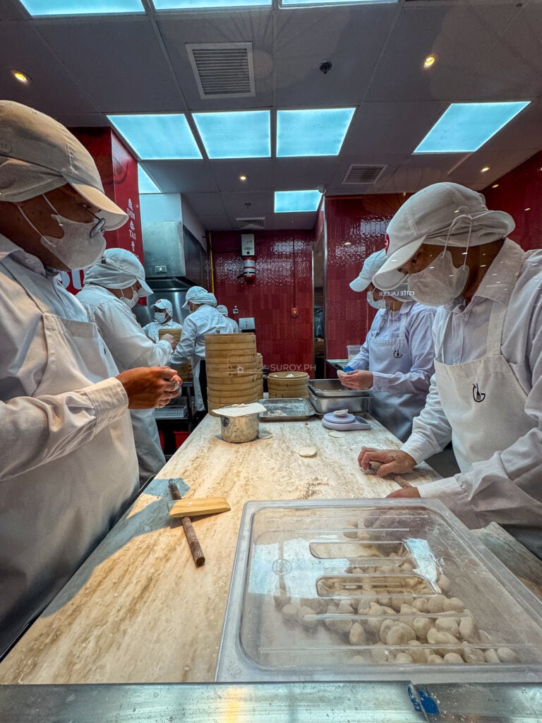 A row of Din Tai Fung cooks in white coats and caps folding xiaolongbao behind glass at SM City Cebu