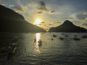 Outrigger boats moored off El Nido town beach at dusk with limestone islands behind