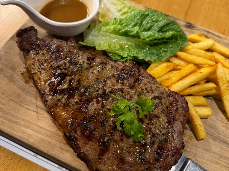 A large grilled steak on a wooden board with fries, romaine and a gravy boat at Fat Jim's Steak House in Mandaue