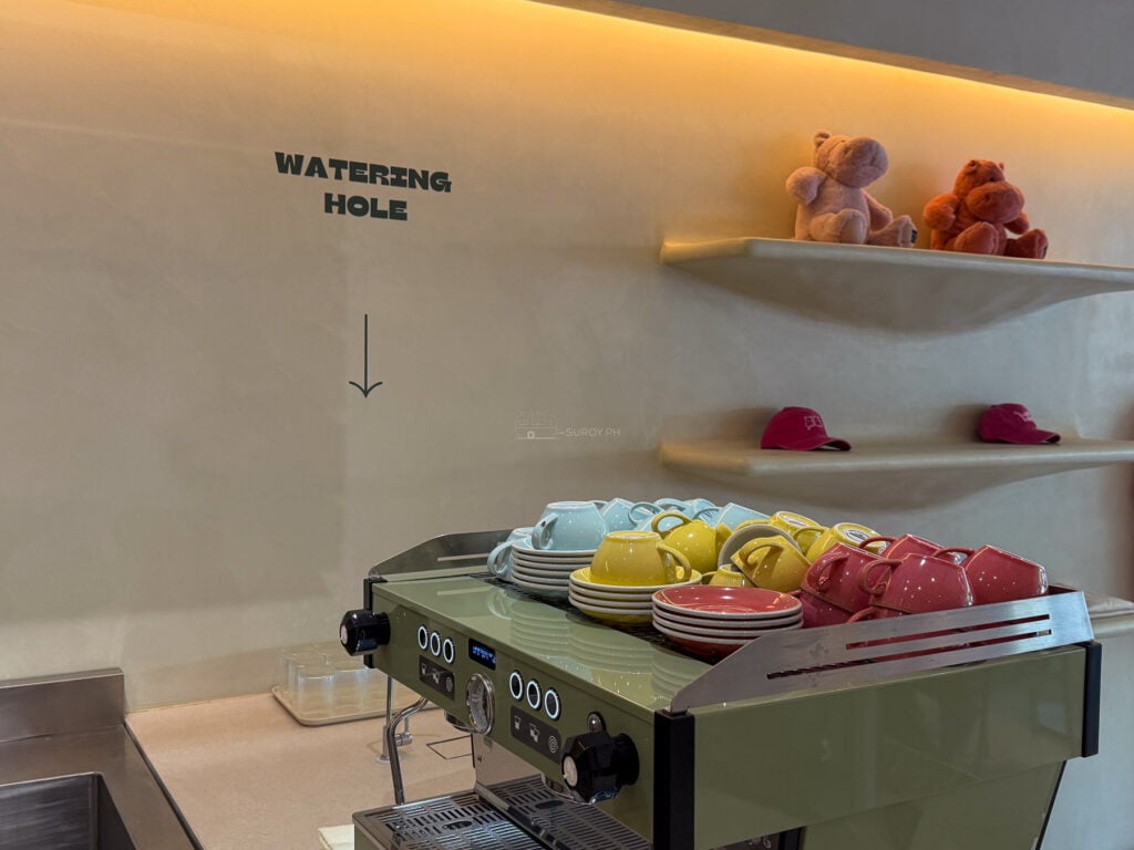 Interior at Happy Hippos Banilad, the espresso machine under a wall sign reading WATERING HOLE with hippo plush toys on the shelf