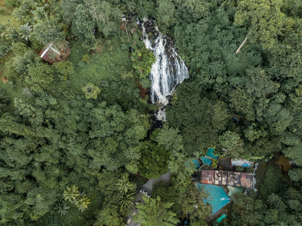 Aerial of Mimbalut Falls with the blue roofed cottages and pools of the resort visible in the trees at the base