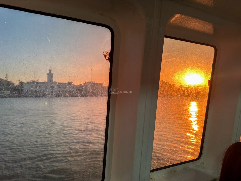 Sunset over the Iloilo Strait seen through the window of a fast craft, with the port skyline on the far bank