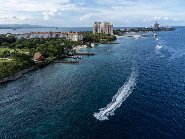 Aerial view of the turquoise reef flat and deep blue drop-off along the Punta Engano coast in Lapu-Lapu City with a jetski wake crossing the frame