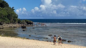 Magpupungko rock pools at low tide in Pilar, Siargao, the reef flats exposed and swimmers wading out to the pools below a tree-lined headland
