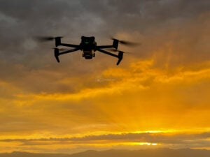 A DJI Mavic 3 hovering in silhouette against a burning orange sunset sky with a mountain ridge below, Philippines