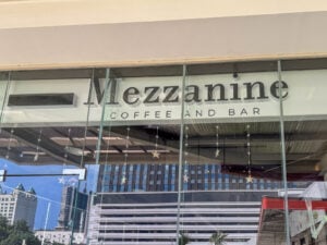 The Mezzanine Coffee and Bar sign on a glass frontage with Cebu tower blocks behind it