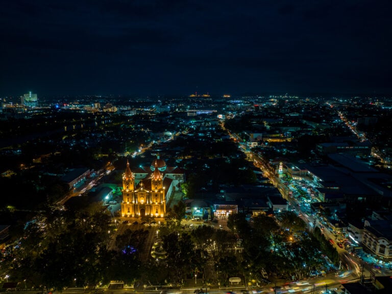 Night aerial of the floodlit Molo Church and Molo Plaza with the lights of Iloilo City stretching to the horizon behind