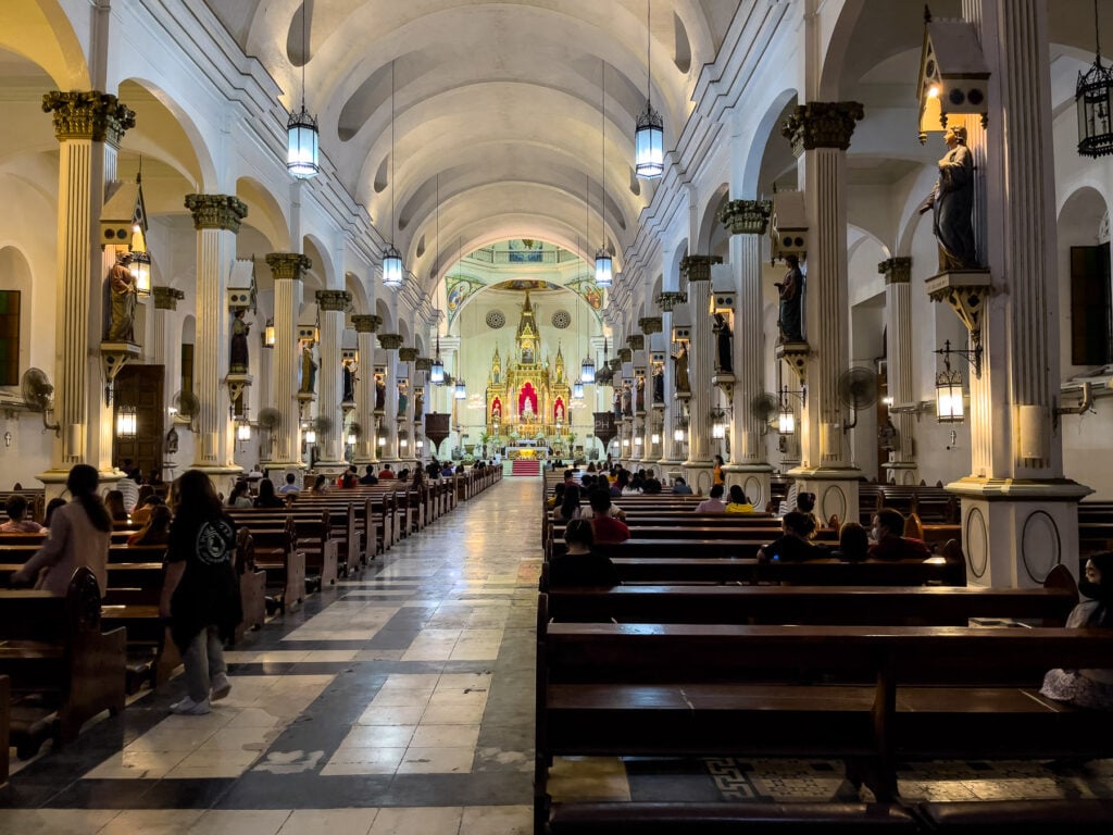 Interior of Molo Church in Iloilo, the nave lined with columns carrying statues of women saints, with worshippers seated in the pews
