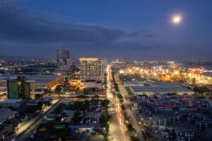 Aerial view at blue hour over the North Reclamation Area in Cebu with the moon above, the Radisson Blu tower lit, and the container port stretching to the right