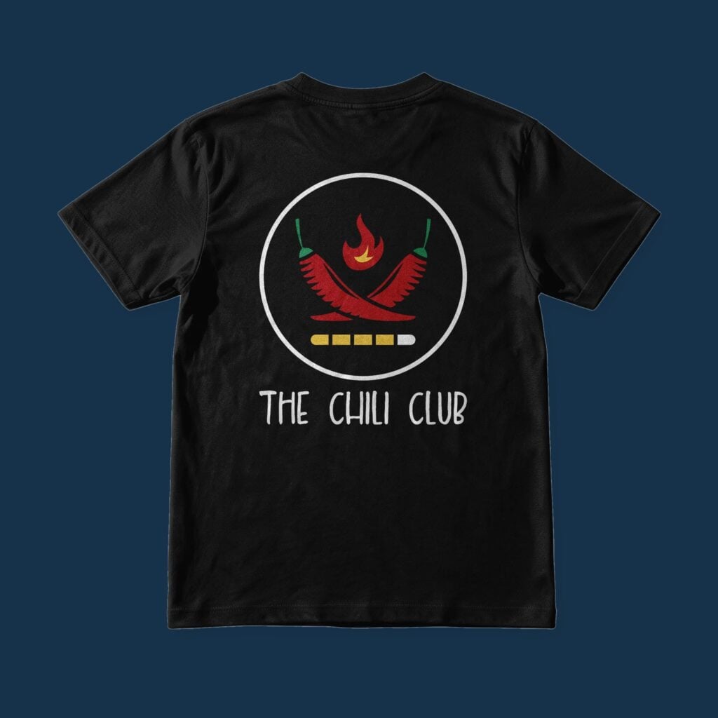 Suroy Wear Chili Club tee in Midnight Black, back view, crossed red chillies under a flame in a ring above a heat scale and the words The Chili Club, on a Reef Navy background
