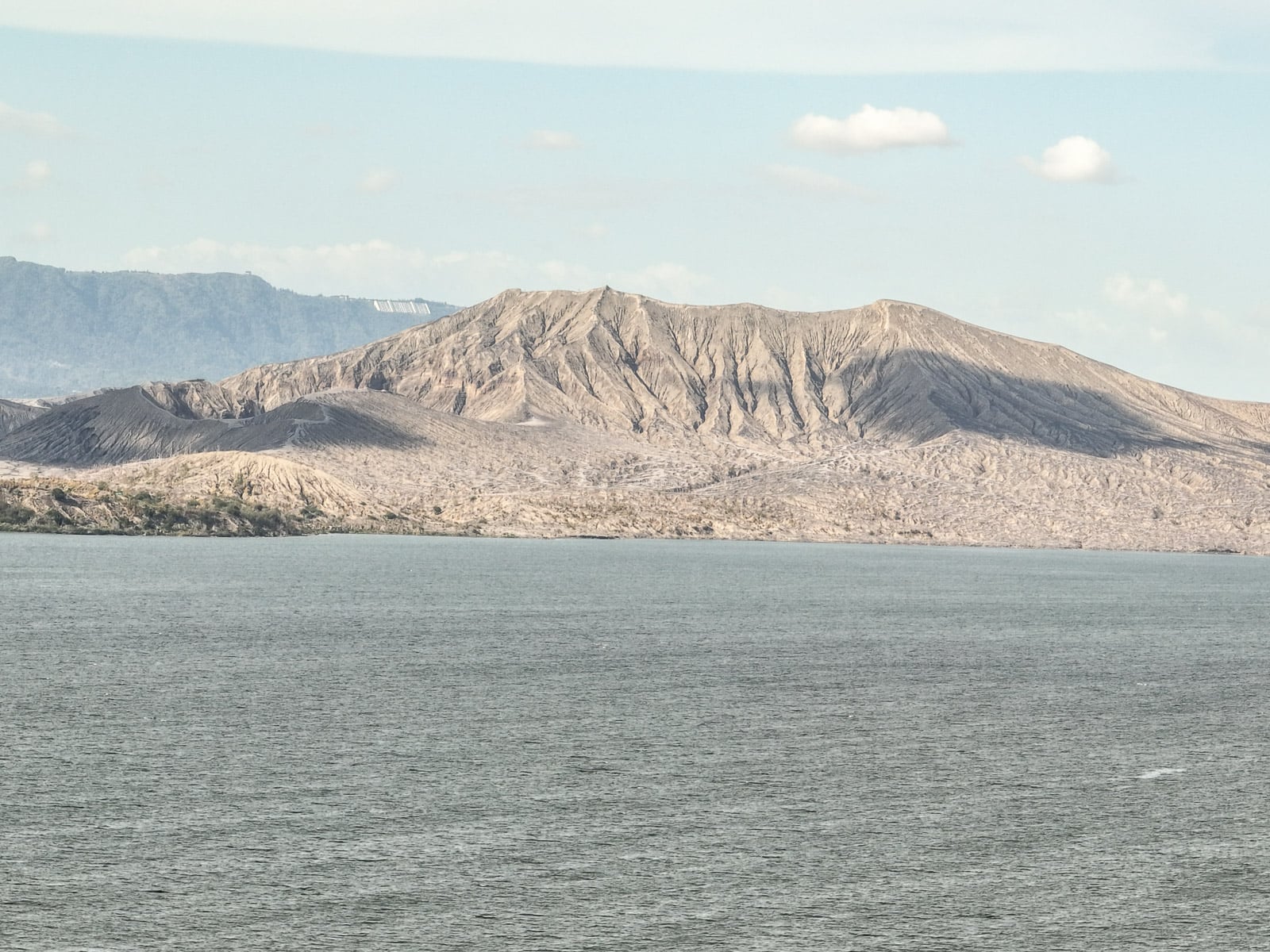 Grey ash covered Taal Volcano crater cone seen across Taal Lake from the southern shore in 2022