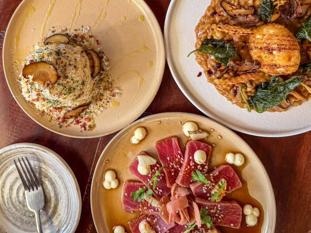 Three plates on a wooden table at Tales and Feelings Cebu including tuna with pickled onion and a grilled dish