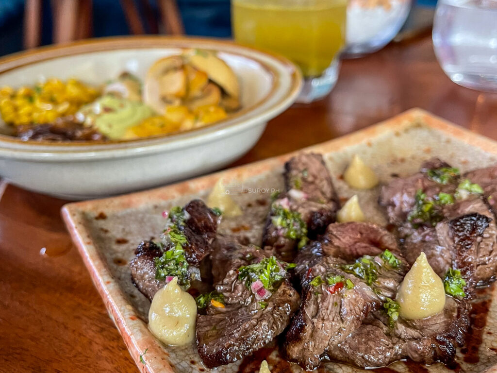 Beef cubes in a line with charred spring onion beside a bowl of mussels and saffron rice at Tales and Feelings Cebu