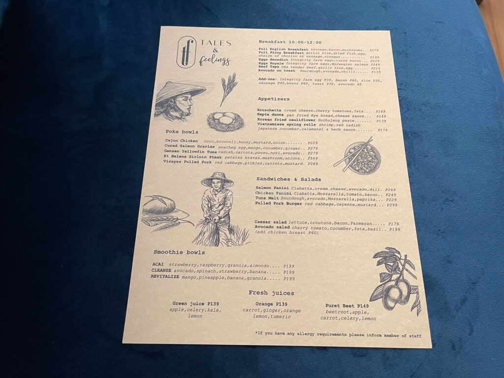 The printed Tales and Feelings Cebu menu page listing breakfast, appetizers, poke bowls and sandwiches with peso prices