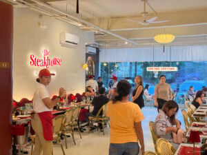Staff in red caps serving a full dining room at The Steakhouse by Carne & Deli on Apitong Street, Cebu City