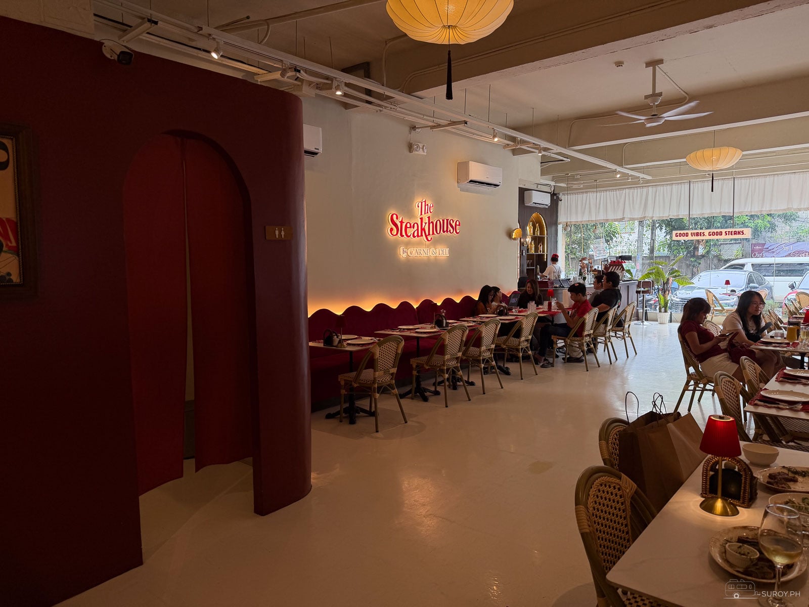 Dining room at The Steakhouse by Carne & Deli in Cebu City with red banquette seating, rattan bistro chairs and the neon logo on a white wall