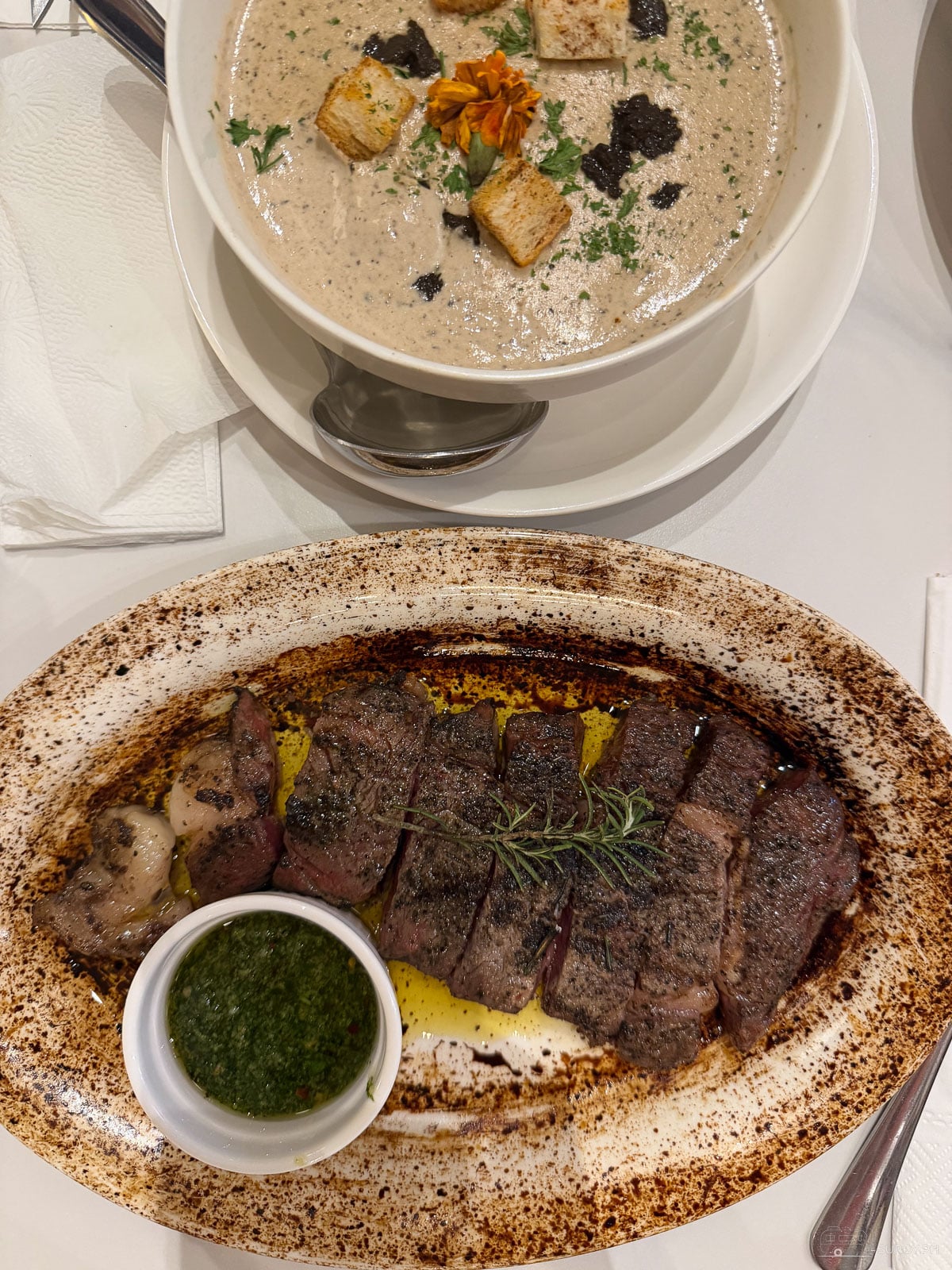 Wild mushroom truffle soup topped with croutons and an edible marigold beside a sliced ribeye at The Steakhouse by Carne & Deli in Cebu